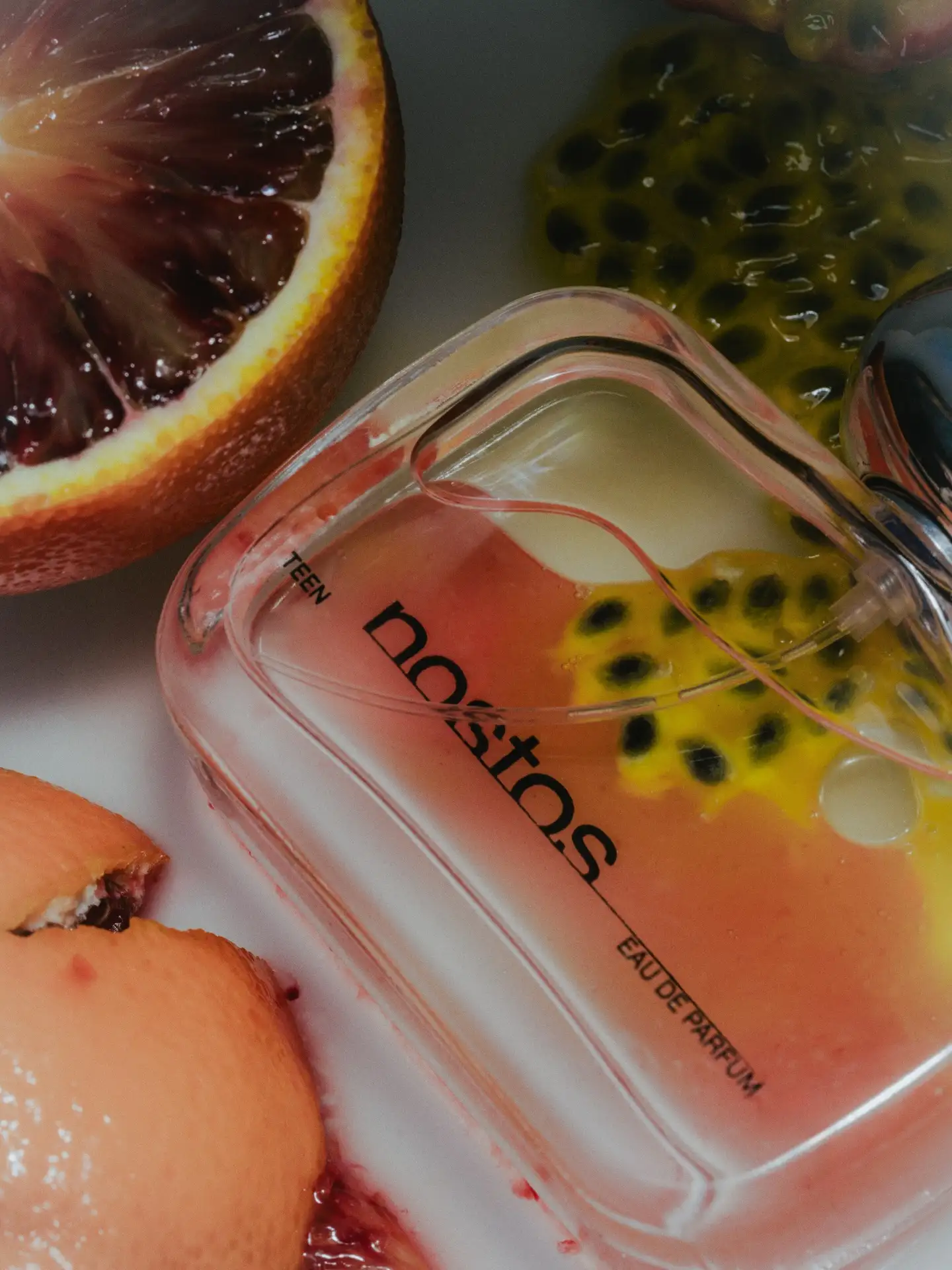 Perfume bottle surrounded by tropical greenery and bright fruits.