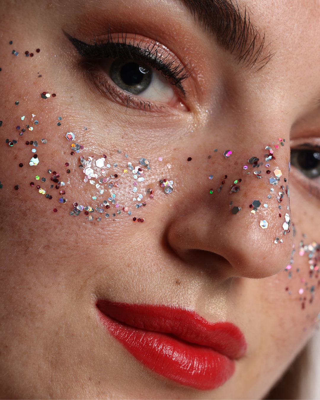 Model with vibrant red lips and iridescent glitter on her cheeks.