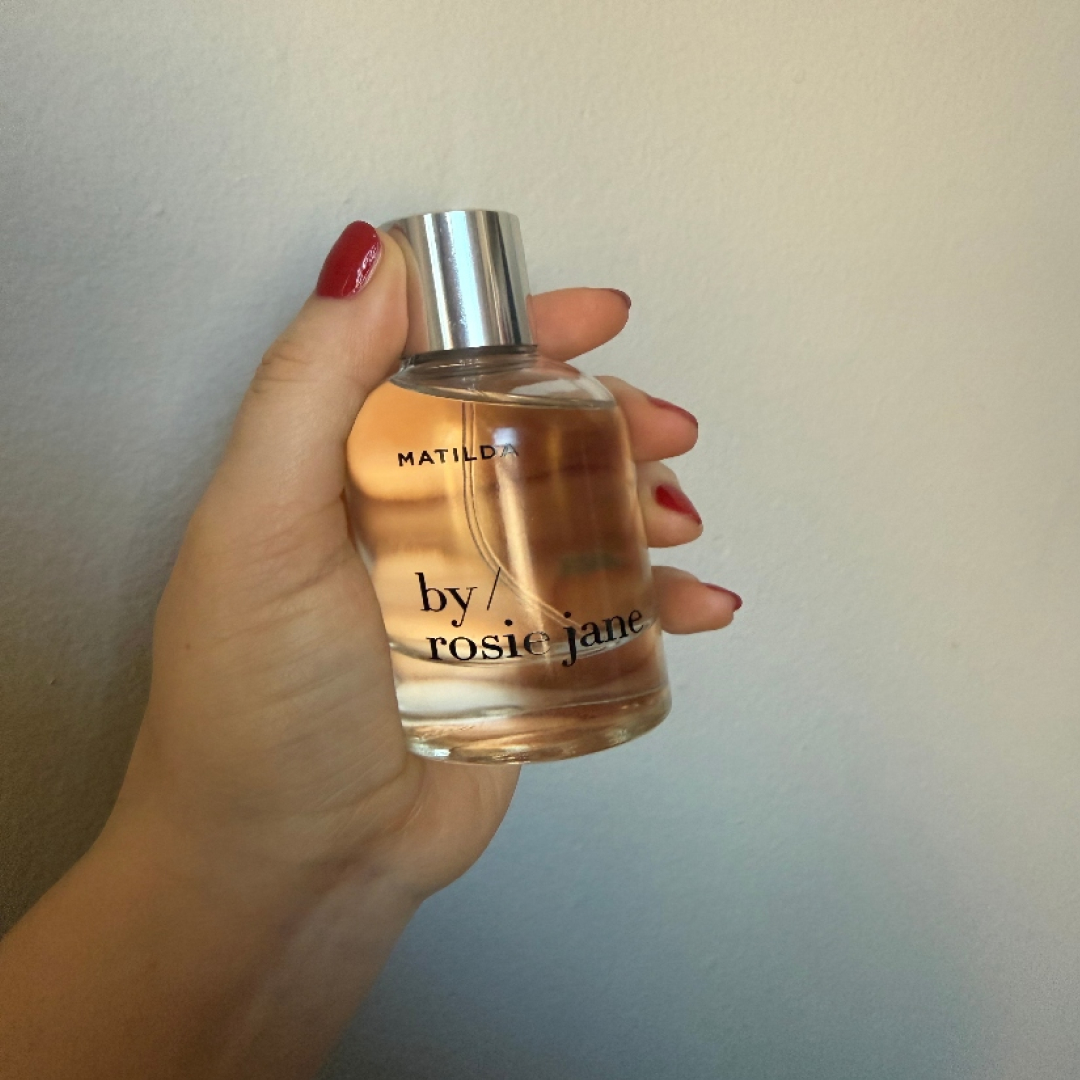A woman holding and smelling a bottle of Matilda perfume.