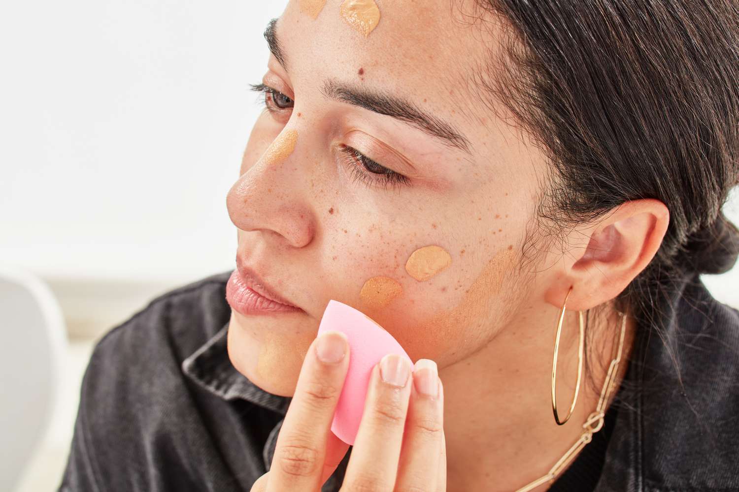 A person applying liquid foundation to their face with a makeup brush.