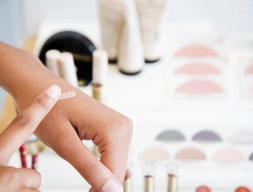 A makeup artist warming concealer on the back of their hand for application.