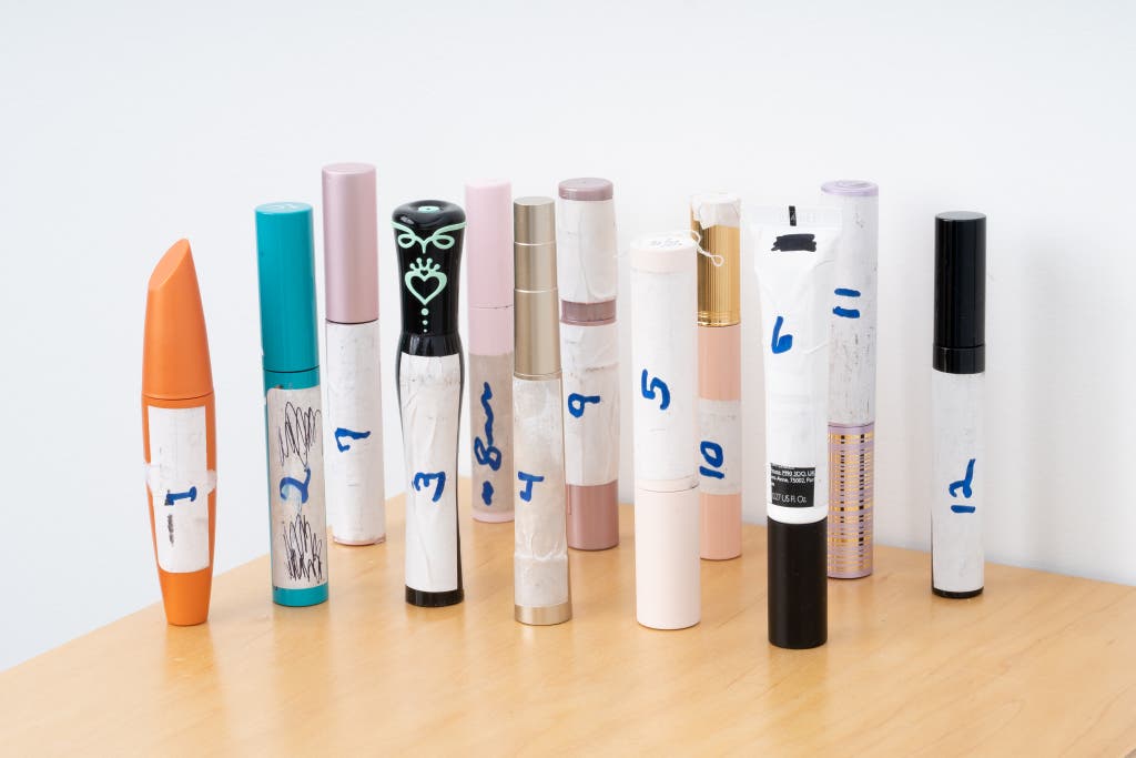 A collection of different mascara tubes with white tape covering the brand names and numbers 1 through 5 written on them for blind testing.