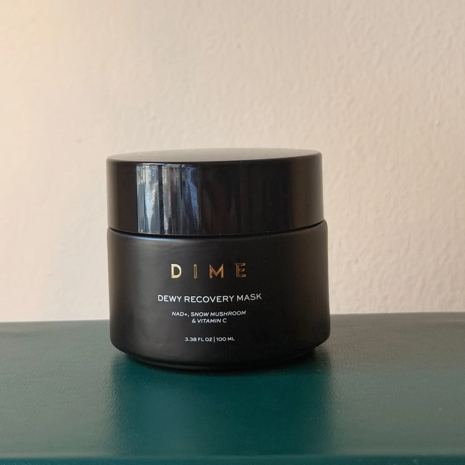 The Dime Dewy Recovery Mask jar sitting on a solid green background.