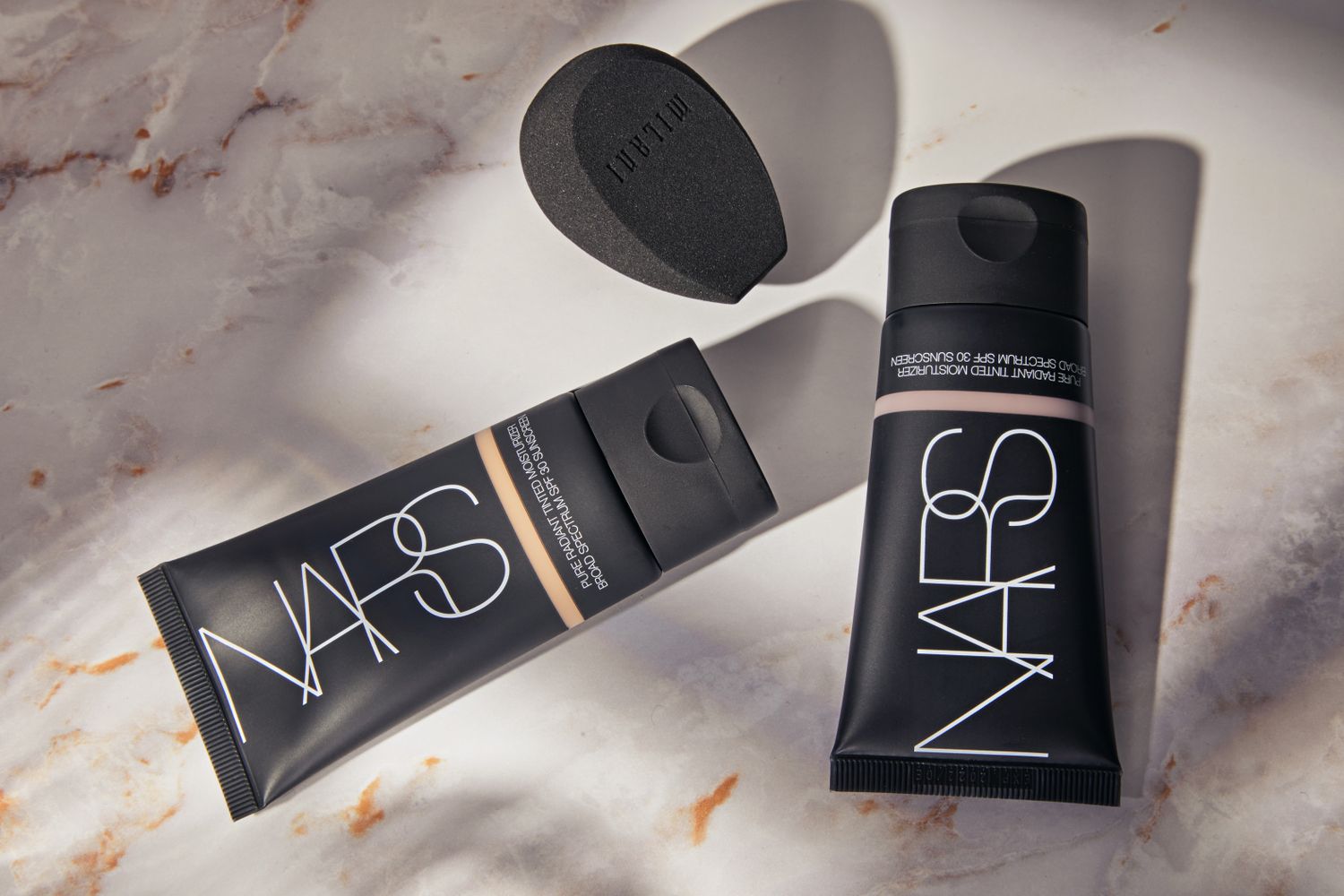 NARS Pure Radiant Tinted Moisturizer tube on a marble surface next to a makeup sponge.