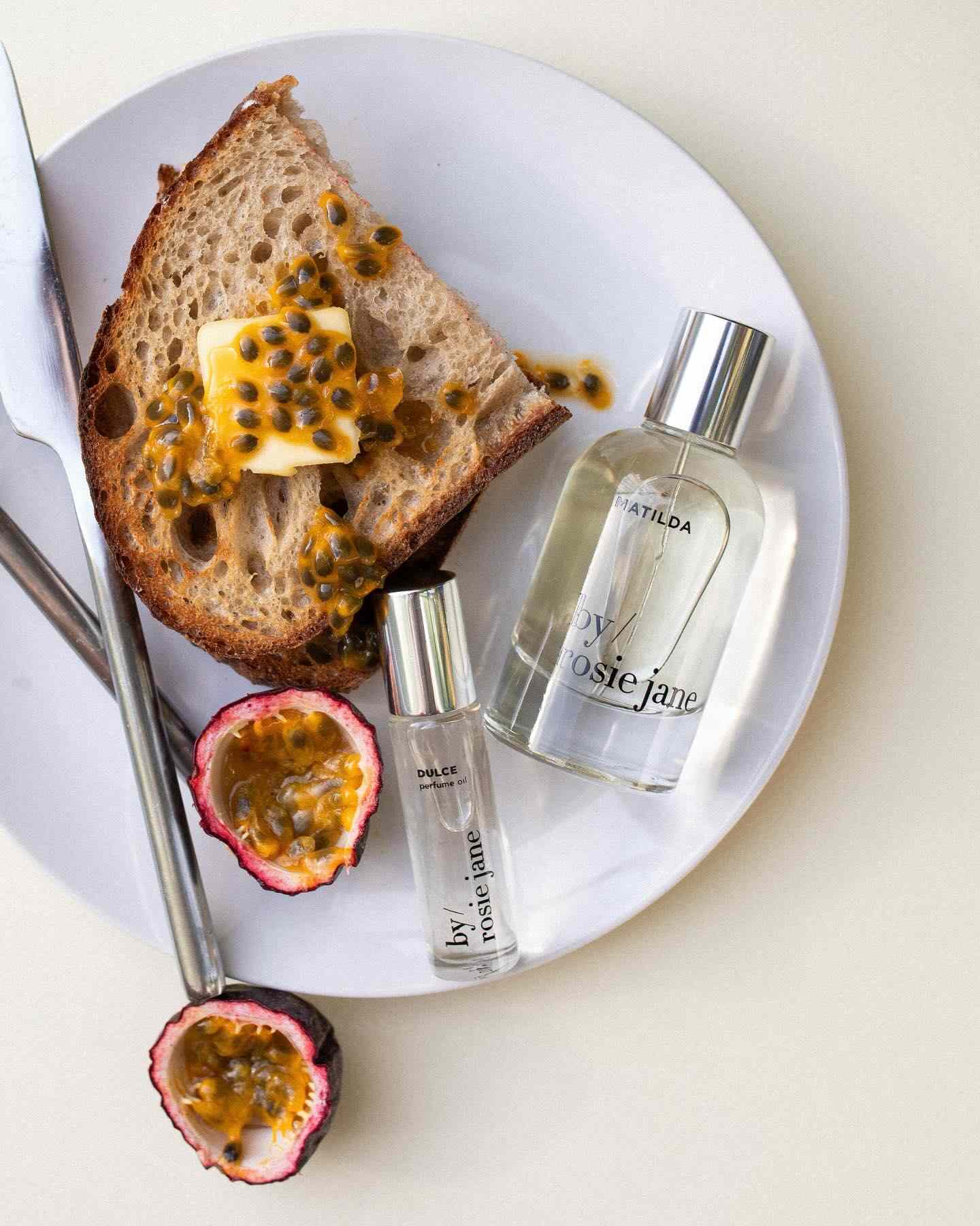 Top-down view of perfume bottles next to passionfruit halves on toast.